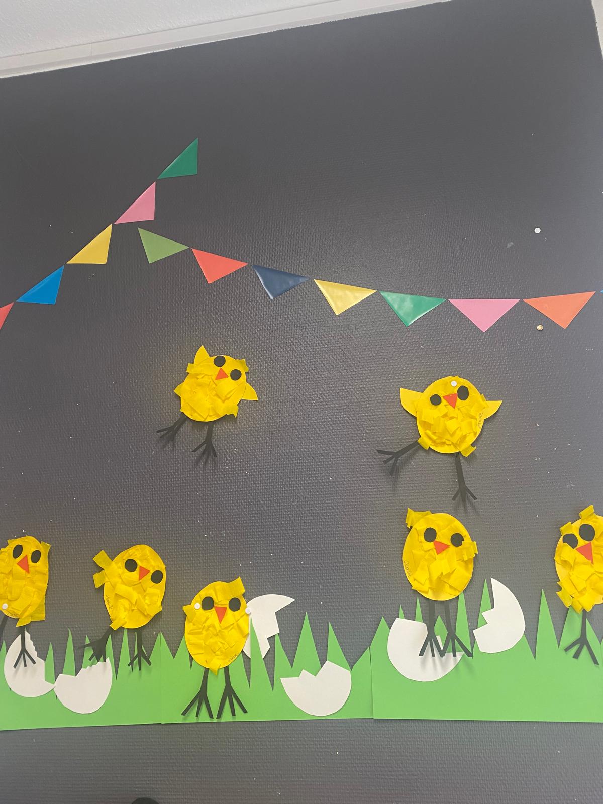 Osterküken aus gerissenem Krepppapier an der Wand, darüber eine Wimpelkette