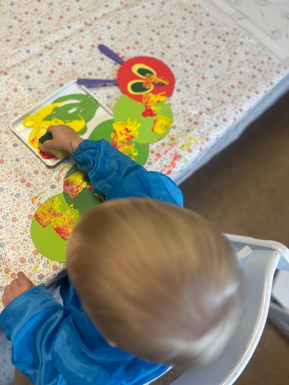 Ein Kind stempelt mit einem Schwamm Farbe auf eine Raupe aus grünen Papierkreisen