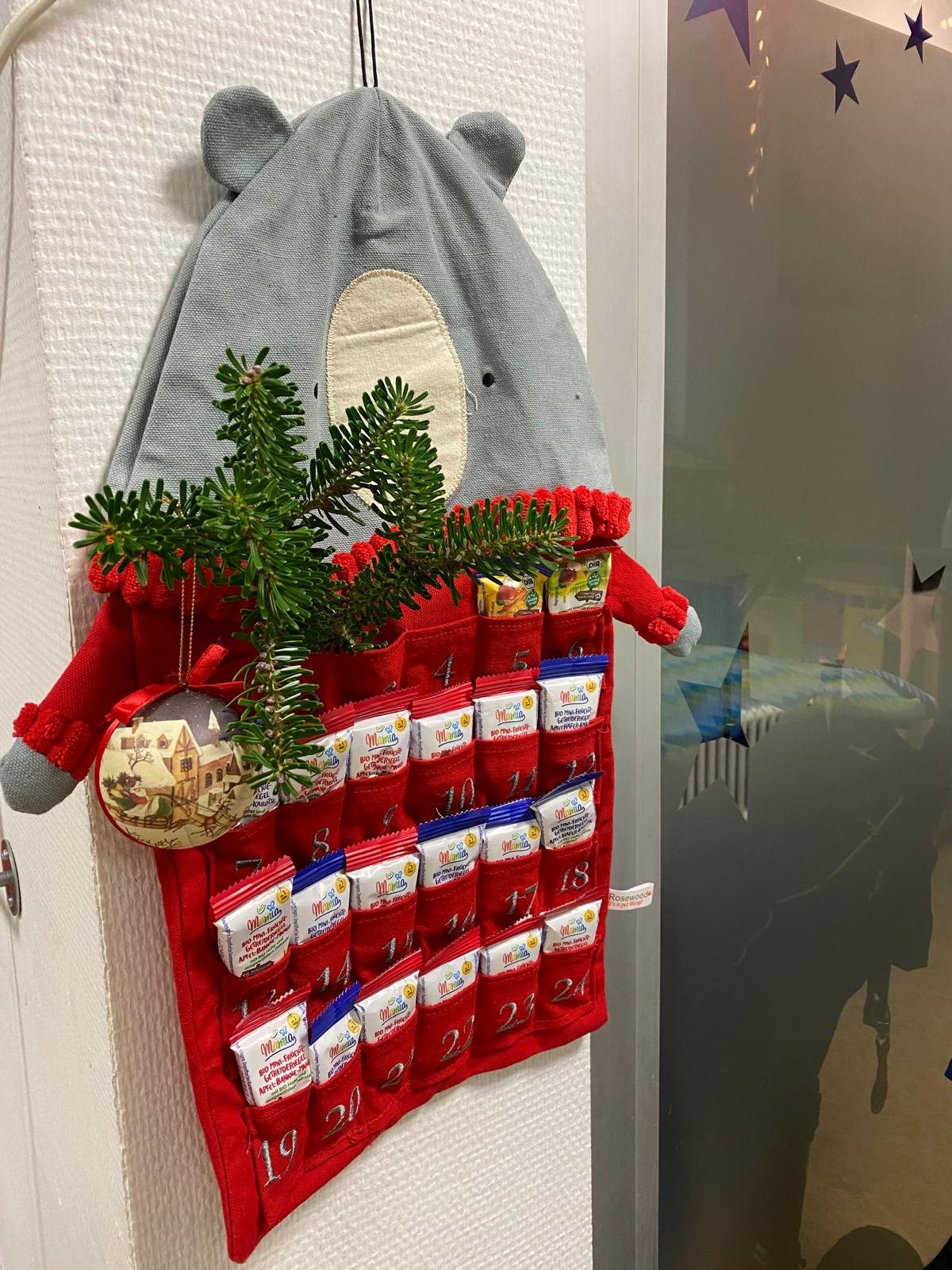 Roter Adventskalender aus Stoff mit Tannenzweigen und kleinen Bärenohren an der Wand
