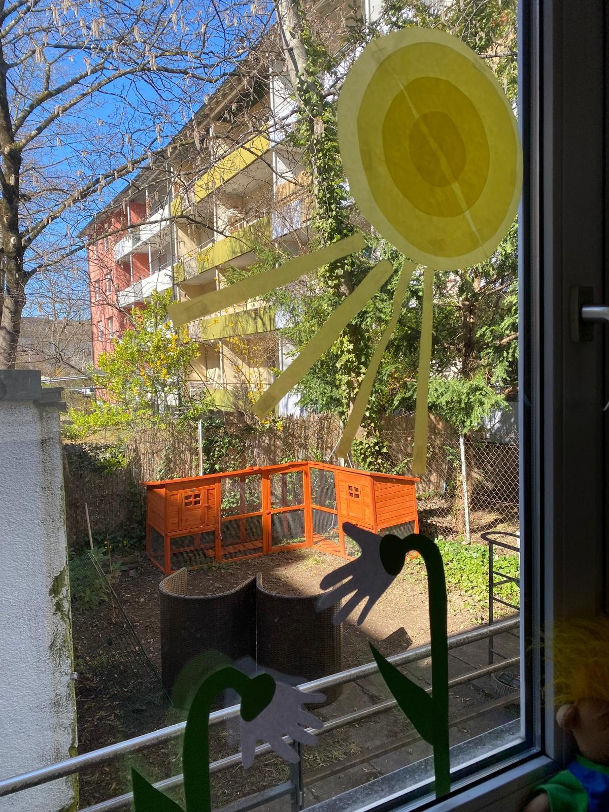 Blick aus dem Fenster in den Garten, am Fenster eine gelbe Papiersonne