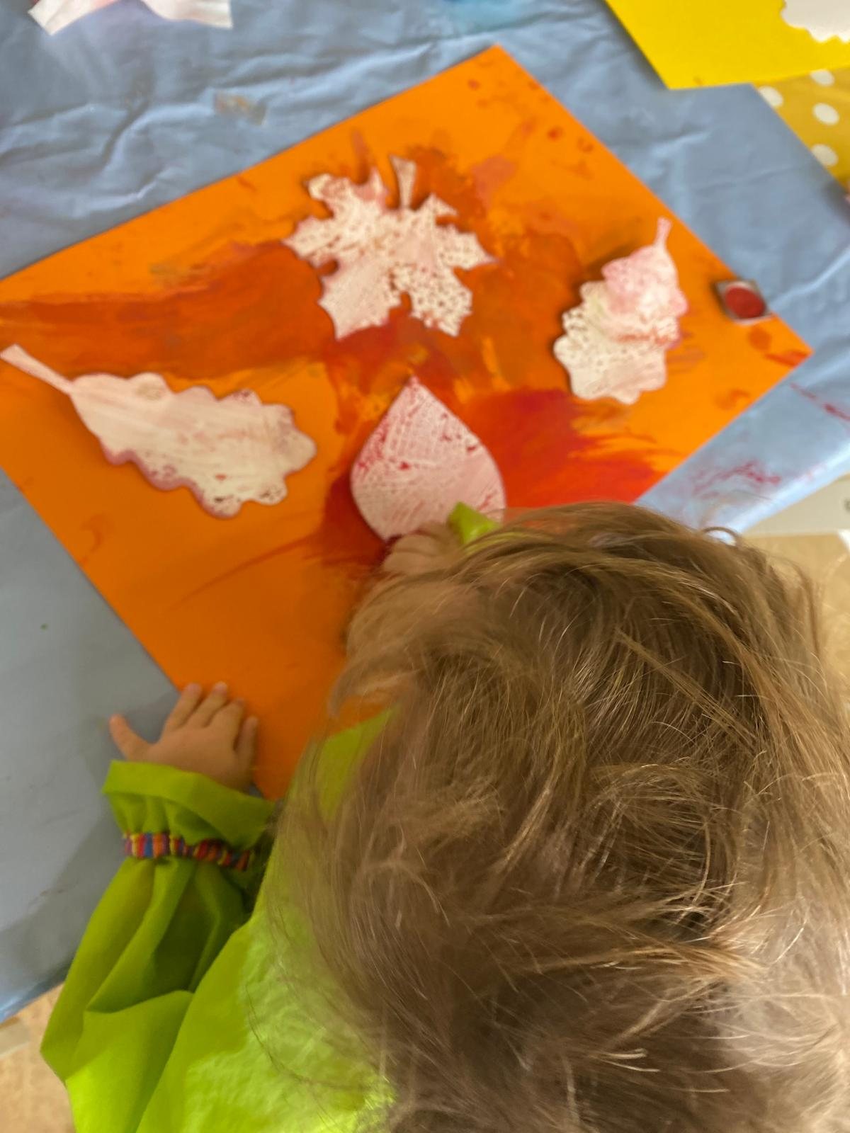 Ein Kind gestaltet ein Bild mit Blätterabdrücken auf orangem Papier