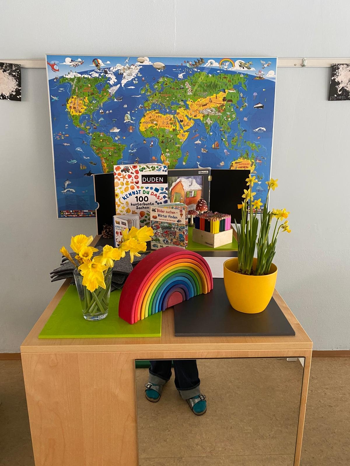 Holztisch mit Holzregenbogen und Narzissen vor einer bunten Weltkarte